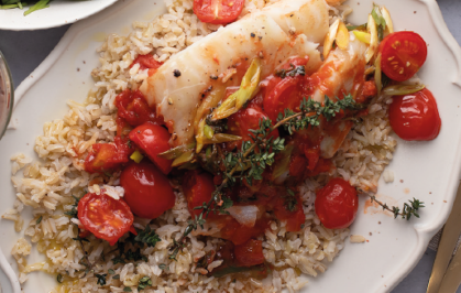 Gericht mit Fisch, Reis und Tomaten auf einem Teller.